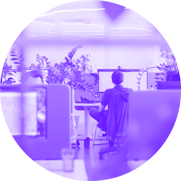 Office environment covered in plants, in the center - person sitting back to camera working at his desk.